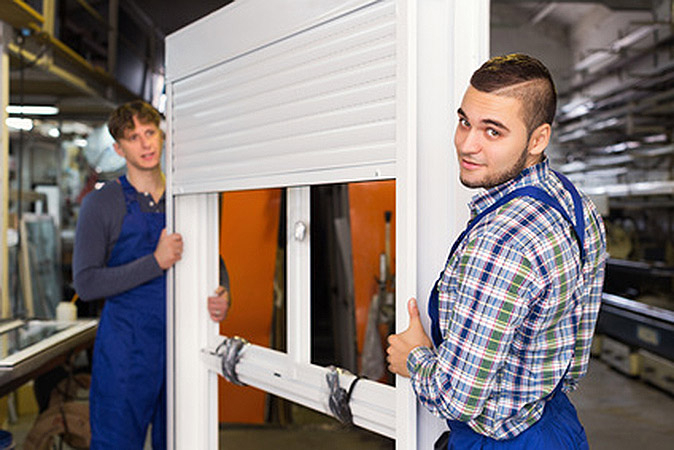 Two young careful workmen inspecting windows with shutter at workshop